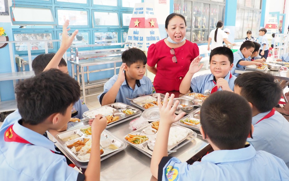 Nhân viên y tế Trường Tiểu học Lê Thị Riêng (phường Hòa Hưng, TPHCM) lắng nghe ý kiến học sinh tại bữa ăn bán trú. Ảnh: THU TÂM